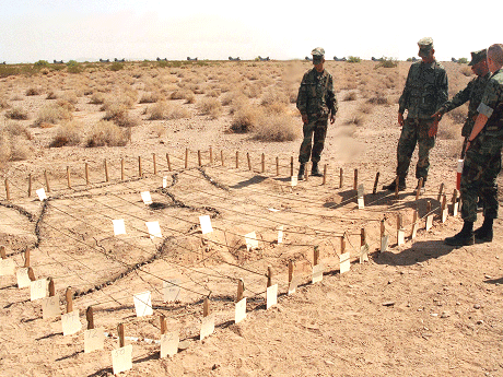 Photo of group of soldiers standing around an outdoor sandbox used for tactical games.