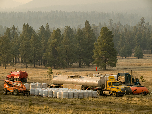 A chemical retardant mixing area in an open field on a fire assignment. Several trucks parked with bags of chemicals lined up and mixing tanks in background.