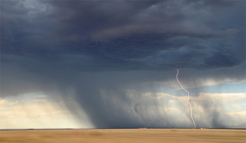 Heavy clouds and rainfall with a bolt of lightning striking dry grass plains. Decorative