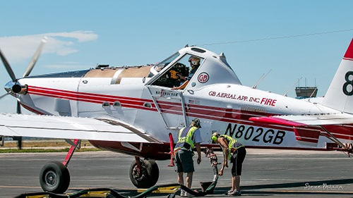 Two tanker base ground crew refuel a single engine airtanker.  Decorative