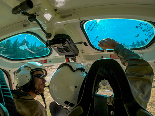 Two helicopter pilots in helicopter. Pilot on right is writing data on upper window. Decorative