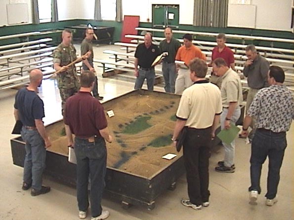 Photo of group of students standing around a sandbox used for tactical games.
