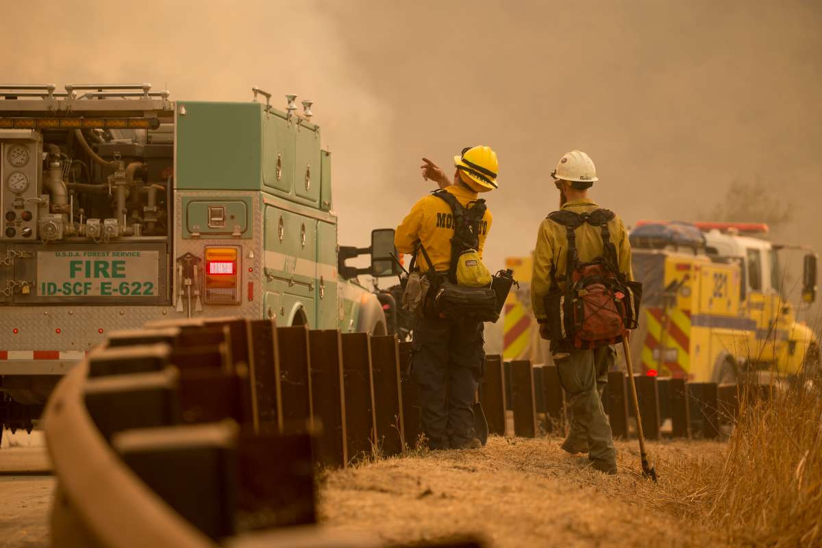 Photo of 2 firefighters on a smoky road with mobile equipment.