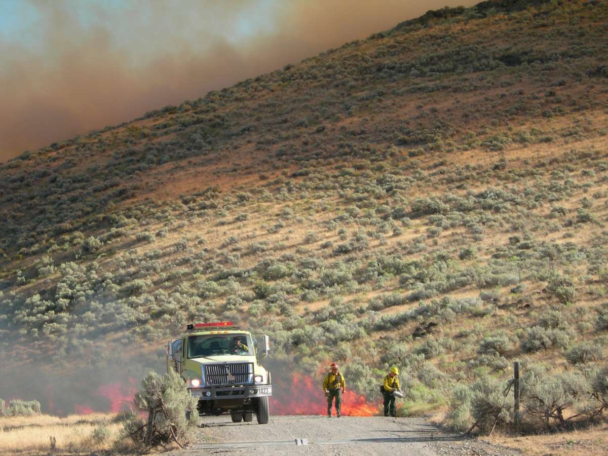 Photo of 2 firefighters on a smoky road with mobile equipment