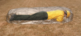 Man in fire-fighter uniform wearing a helmet, laying on top of fire-shelter across the length of the shelter.