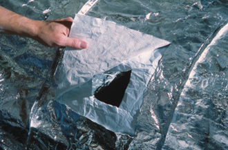 A person's hand pulling a cutaway to show the inner and outer shell of a fire shelter.