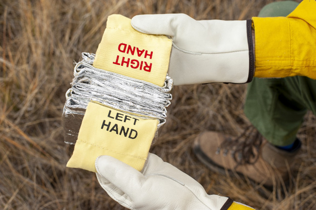 The hands of a firefighter wearing gloves are holding a the left and right handles of a shelter.