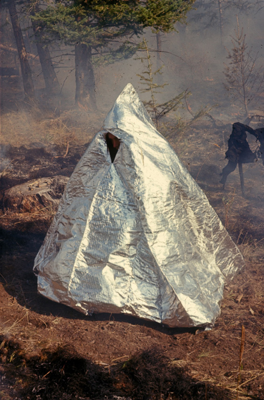 Man inside of a bell-shaped shelter made of a laminate of aluminum foil and glass cloth in the forest.