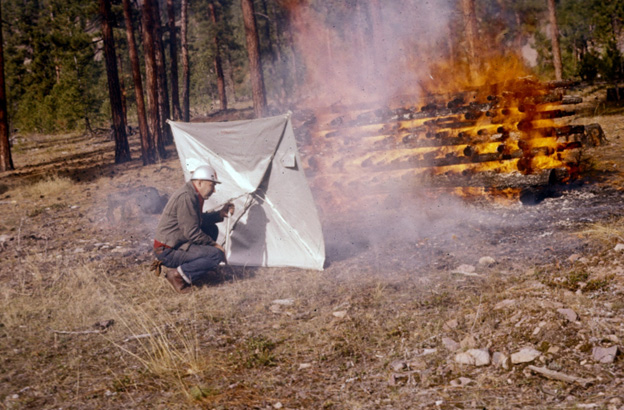 Man in squatting position holding a heatshield between himself and a controlled fire.