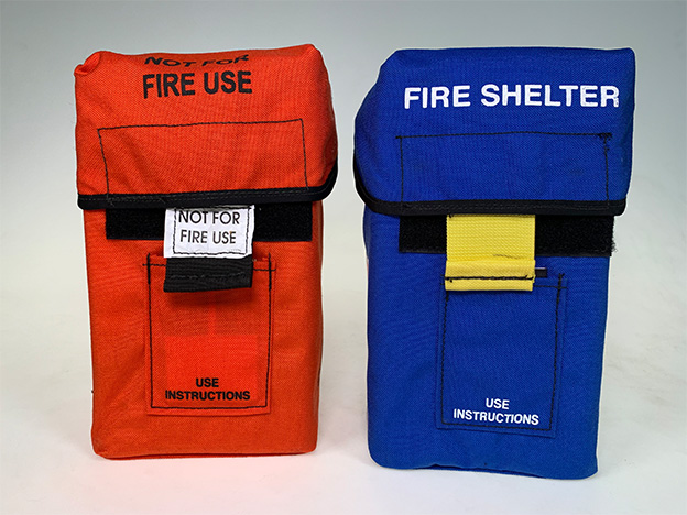 Practice shelter carriers side-by-side one red, the other blue.  Red carrier has labels: Not for Fire Use and Use Instructions.  Blue carrier has labels Fire Shelter Use Instructions 