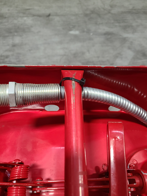 Closeup of the top of a fuel can with the hose zip tied to the handle.