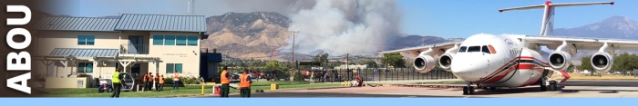 ABOU decorative banner. An airtanker sits on the tarmac of an airtanker base while people look at the burning mountains in the distance.