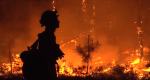 Silhouette of fire fighter standing in front of burning timber.