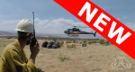Man wearing hardhat, holding radio while watching a helicopter land in the distance.