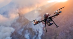 Image of a drone flying in the sky above smoke filled mountains.