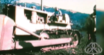 An old dozer with operator at controls and a firefighter walking to right out of frame.