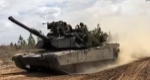 An armored tank drives across dirt.