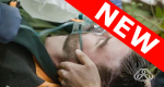 Man laying on ground with oxygen mask on and a hand holding his head.