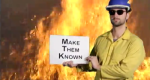 Fire fighter standing in front of flames holding sign that says "make them known".