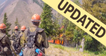 Group of wildland firefighters stand on hill looking down at flames in trees. With "UPDATED" banner.