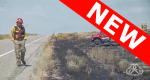 Firefighter walking on side of road looking at a burned out area with a fire truck sitting in burned out area in the distance.